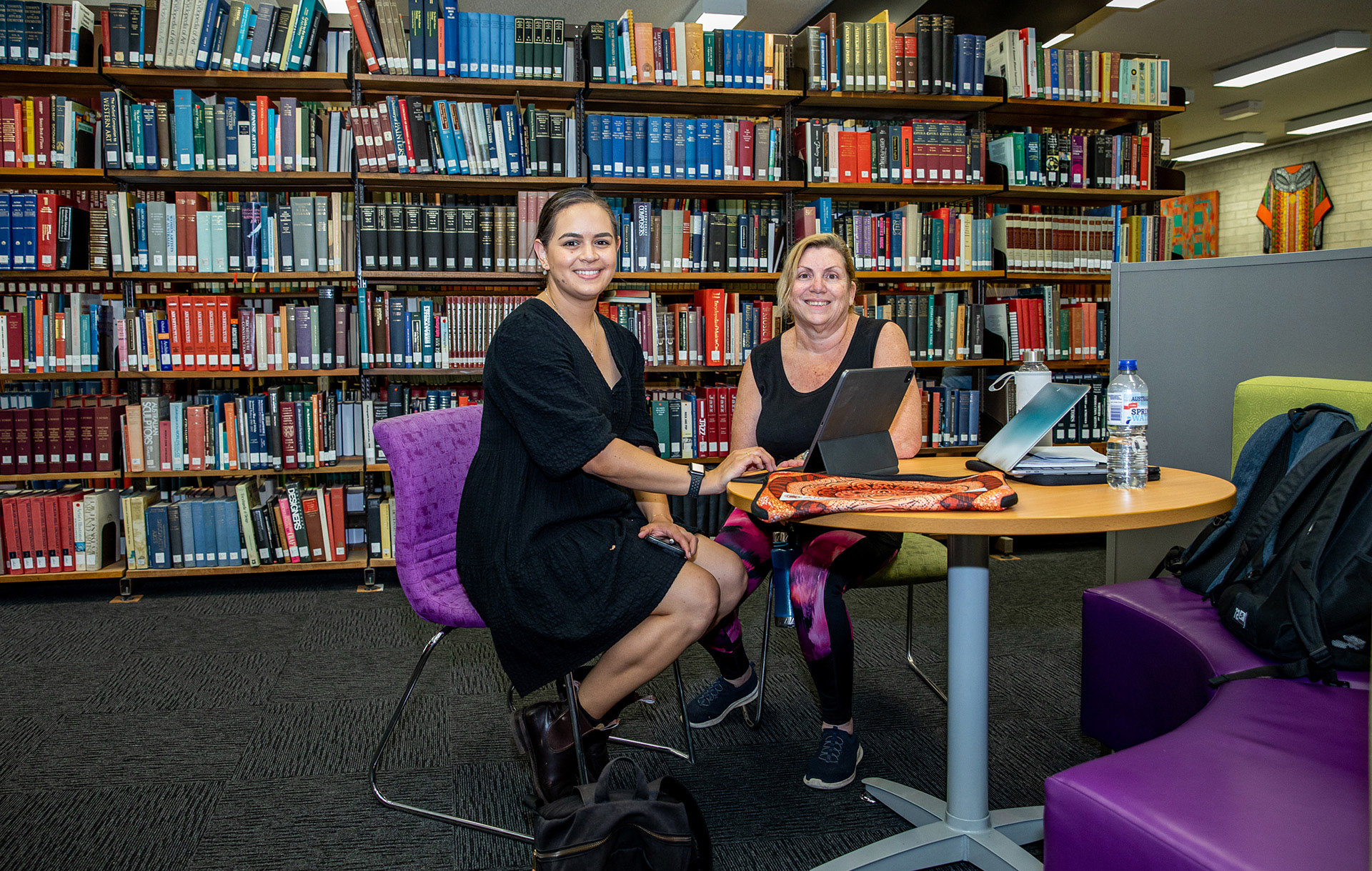 两位成年女性坐在JCU校园的办公桌旁,周围环绕着书籍